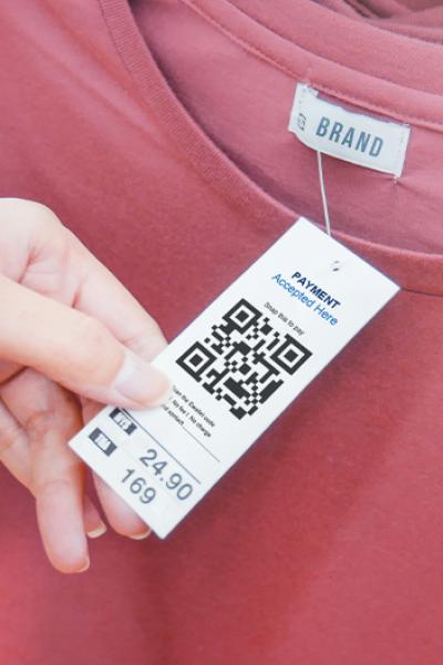 woman-s-hand-with-cloth-hang-tag-label-with-qr-code-in-clothing-shop