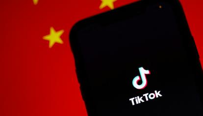 Fotografía referencial de un celular con el logo de TikTok en su pantalla mientras en el fondo se ve parte de una bandera china.