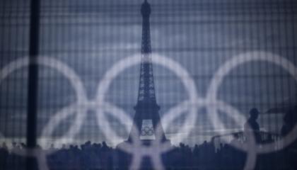 Los visitantes pasan junto a una pancarta con anillos olímpicos colocada sobre una barrera con la Torre Eiffel al fondo, el 16 de julio de 2024.