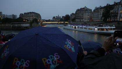 Miembros del público se protegen de la lluvia con paraguas mientras observan el desfile de las delegaciones por el río Sena.