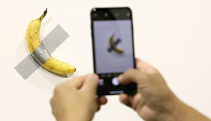 Una persona tomando foto al plátano pegado en la pared.