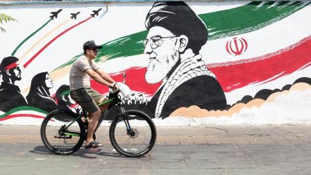 Persona anda en bicicleta frente a un mural de propaganda contra la guerra en Teherán, Irán, el 13 de agosto de 2026.