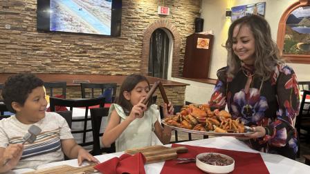 Mateo y Abby reciben una bandeja de cangrejos de manos de Nancy de Pardo, una de las propietarias de Sabor Latino. Los dos niños conocieron esta tradición ecuatoriana en Estados Unidos, lejos del país donde creció su familia.