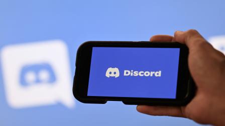 Una mano sosteniendo un teléfono inteligente frente a una pantalla con el logotipo de la empresa estadounidense Discord, 12 de agosto de 2026.