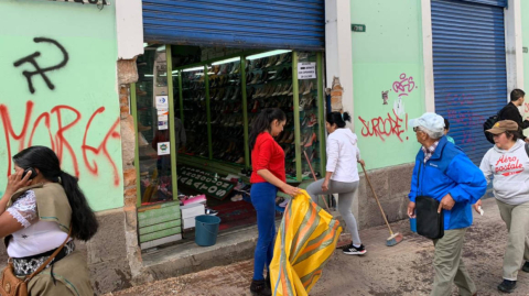 Ciudadanos limpian los exteriores de un negocio afectado por las protestas en el Centro Histórico de Quito.