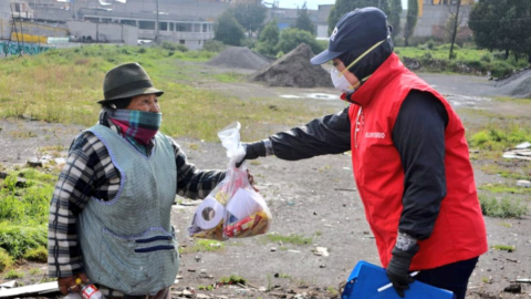 Un funcionario del Municipio de Quito entrega un kit de alimentos a una mujer, en el sur de Quito, el jueves 26 de marzo de 2020.