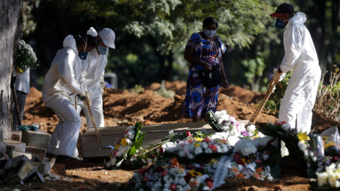 Empleados cargan un ataúd de una persona, durante su funeral. este 29 de abril, en un cementerio de Sao Paulo.