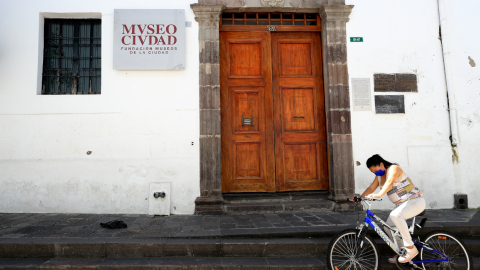 Una mujer con mascarilla y en bicicleta pasa frente al Museo de la Ciudad, en Quito, el domingo 17 de mayo de 2020.