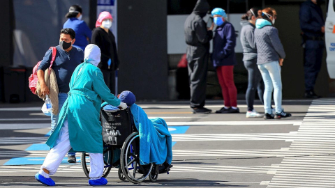 Familiares de pacientes diagnosticados esperan información mientras ingresa un paciente en silla de ruedas a un hospital en Quito, 13 de julio de 2020.