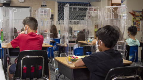 Niños de una escuela en Estados Unidos en pupitres con divisores de acrílicos, el 24 de agosto de 2020.