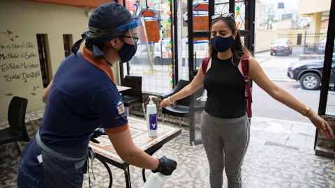 Una mujer aplica alcohol a una cliente antes de entrar a un establecimiento en Quito, 7 de julio de 2020.