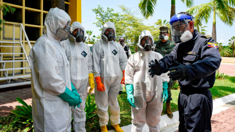 Personal de limpieza con trajes de bioseguridad y mascarillas escucha indicaciones de un guardia, el 19 de octubre de 2020.