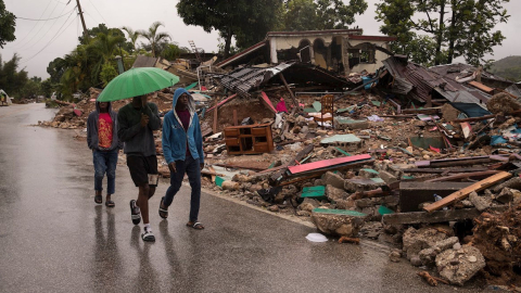 Hombres caminan junto a una casa destruida, mientras cae la lluvia que deja el paso de la tormenta Grace, 17 de agosto de 2021.