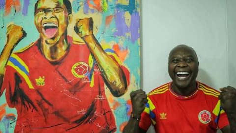 Freddy Rincón sonríe posando la camiseta de la selección colombiana junto a cuadro en donde aparece su imagen.