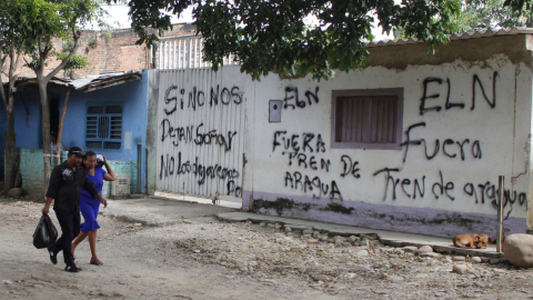 Una pareja camina junto a una pared llena de grafitis alusivos al grupo guerrillero ELN, en Colombia, el 20 de mayo de 2022. 