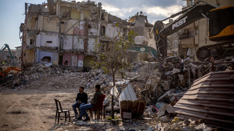 Ciudadanos turcos descansan frente a los escombros, en la ciudad de Hatay.