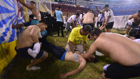 Aficionados auxilian a una persona tirada en el piso durante una estampida en El Salvador, el 20 de mayo de 2023.