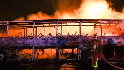 Un bombero apaga el incendio de un bus causado por manifestantes en Nanterre, Francia.