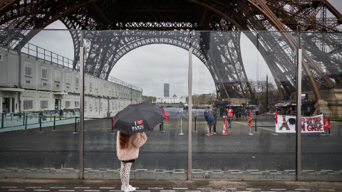 Un peatón con un paraguas que dice "Amo París" mira junto a la Torre Eiffel y una pancarta (R) que dice "empleados de la Torre Eiffel en huelga" en París el 19 de febrero de 2024.