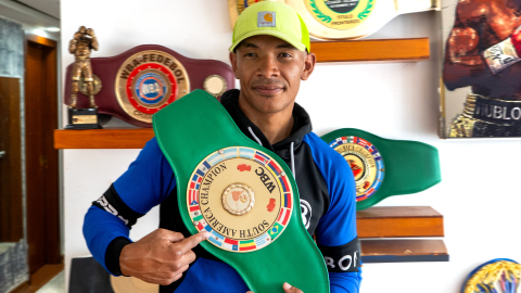 El boxeador Erick Bone posa en la sala de su casa con el primer cinturón que ganó en su carrera.