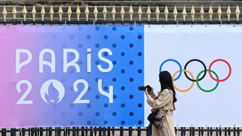 Transeúnte toma una fotografía de una pancarta de los próximos Juegos Olímpicos de París 2024 frente a la Asamblea Nacional en París, el 5 de mayo de 2024.