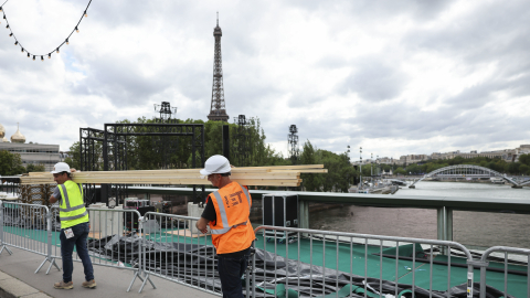 Varios operarios pasan ante el río Sena de París, escenario elegido para la ceremonia de inauguración de los Juegos Olímpicos el próximo viernes 26 de Julio.