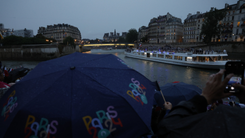 Miembros del público se protegen de la lluvia con paraguas mientras observan el desfile de las delegaciones por el río Sena.