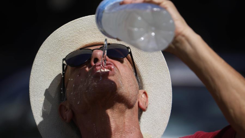 Un hombre se refresca con agua de una botella mientras camina por el Puente Romano de Córdoba, 9 de agosto de 2024.