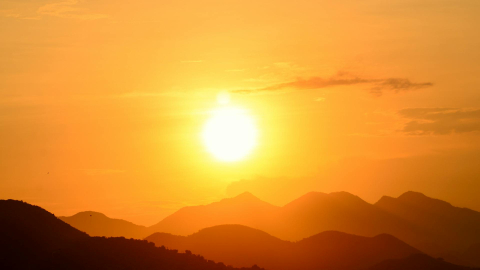 Fotografía referencial de un sol intenso sobre montañas en un cielo con pocas nubes.