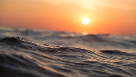 Fotografía referencial del océano mientras el Sol se esconde en el horizonte, en un día de calor.