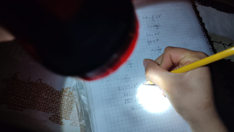 Una estudiante se apoya con una linterna recargable para realizar tareas, durante los cortes de luz en Quito.