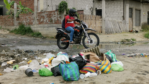 Una motocicleta atraviesa un pozo de aguas servidas donde se acumula un montículo de basura en la cooperativa San Francisco, al norte de Guayaquil, territorio del grupo criminal Los Lobos.