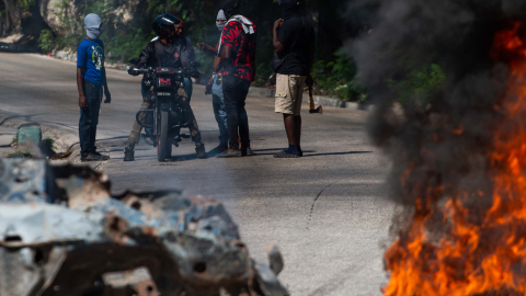 Fotografía de archivo de residentes y motorizados que conversan mientras los restos de cuerpos de personas son quemados en la vía pública, en el suburbio de Petiton-Ville, en Puerto Príncipe, el 19 de noviembre de 2024.