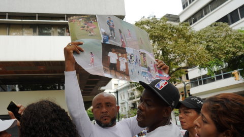 Luis Arroyo, padre de dos menores desaparecidos tras operativo militar en el sur de Guayaquil, levanta una pancarta con fotos de sus pequeños en los exteriores de la Fiscalía del Guayas, en el centro de Guayaquil, en medio de una protesta el lunes 23 de diciembre del 2024