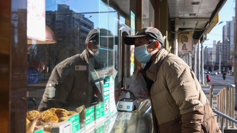 Un adulto mayor utiliza una mascarilla mientras compra comida en un restaurante en Pekín, China, el 6 de enero de 2025.