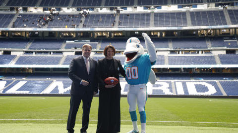 Brett Gosper, director de la NFL en Europa y Asia-Pacífico y Pri Shumate, vicepresidenta de los Miami Dolphins, en el césped del estadio Santiago Bernabéu con la mascota del equipo, durante el acto celebrado este viernes 17 de enero en Madrid en el que la NFL, la Liga profesional de fútbol americano, ha anunciado que los Miami Dolphins serán el 'equipo designado' (local) en el partido de ese campeonato que se disputará este año en el mencionado estadio de la capital.