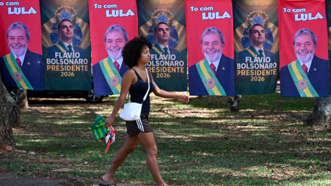 Una mujer pasa junto a banderas y toallas —a la venta en una calle de Brasilia el 22 de octubre de 2026— que exhiben las imágenes del presidente de Brasil y candidato presidencial, Luiz Inácio Lula da Silva, y del senador de derecha y también candidato presidencial, Flávio Bolsonaro.
