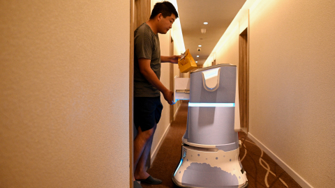 Un cliente recoge su pedido de un robot frente a su habitación en un hotel, el 3 de julio, en Pekín.