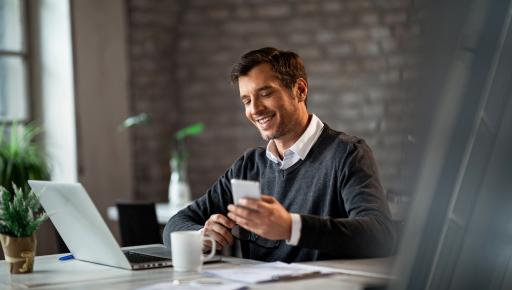 Empresario feliz trabajando con una computadora y un smartphone.