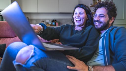 Pareja observa contenido en una laptop mientras comparte un momento en casa.