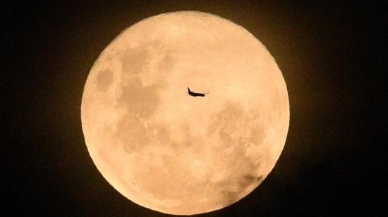 La silueta de un avión se perfila sobre la superficie de la luna llena, en Sídney, Australia.