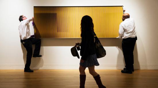 Una mujer pasa junto a trabajadores que cuelgan la escultura Fisicromía Nro 2178 del artista Carlos Cruz-Diez en Sotheby's en Nueva York. 22 de mayo de 2014.