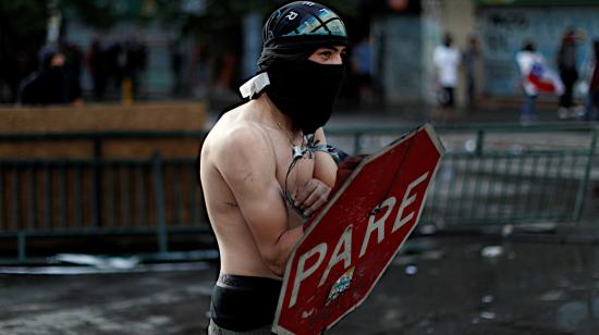 Un manifestante utiliza un signo 'pare' como escudo durante las protestas en Chile.