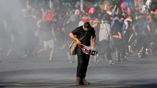 Un manifestante toca el tambor mientras otros manifestantes son dispersados con cañones de agua en las protestas en Chile, en octubre de 2019. 