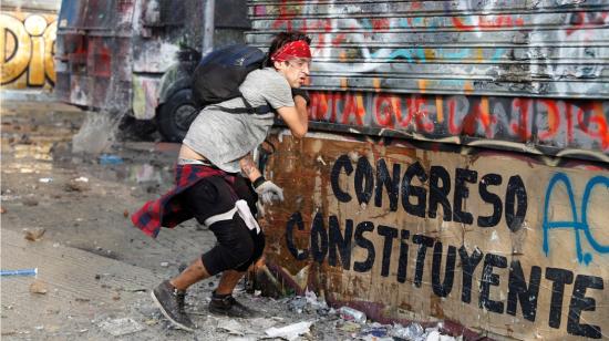 Un manifestante lanza una piedra junto a un cartel con la leyenda "Congreso Constituyente".