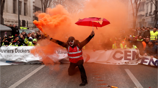 En París, un manifestante con la cara pintada de payaso, activa una bomba de humo durante una protesta.