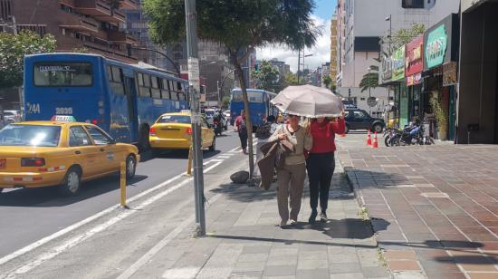 Personas se protegen del sol con paraguas en las calles de Quito.