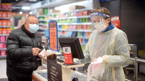 La cajera de un supermercado de la ciudad de Wuhan atiende con mascarilla y otras medidas de protección a un cliente el 10 de febrero de 2020.