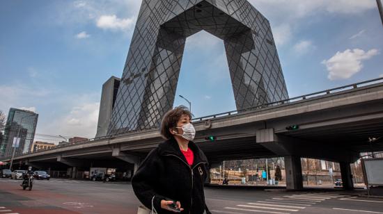 Una mujer con una máscara facial protectora camina junto al edificio de la Televisión Central de China (CCTV)  en Beijing.