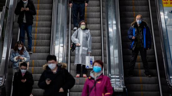 Una mujer con máscara, gafas y impermeable usa una escalera mecánica en la estación de metro de People's Square, en Shanghai, China. 